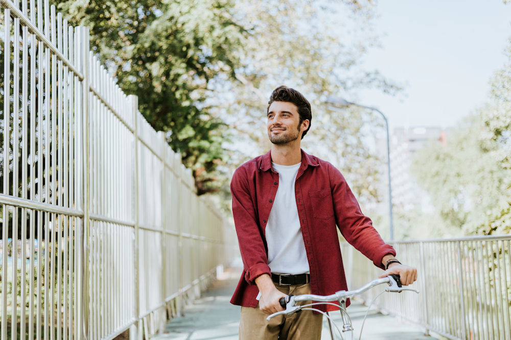 man walking outside along a fence with his bike