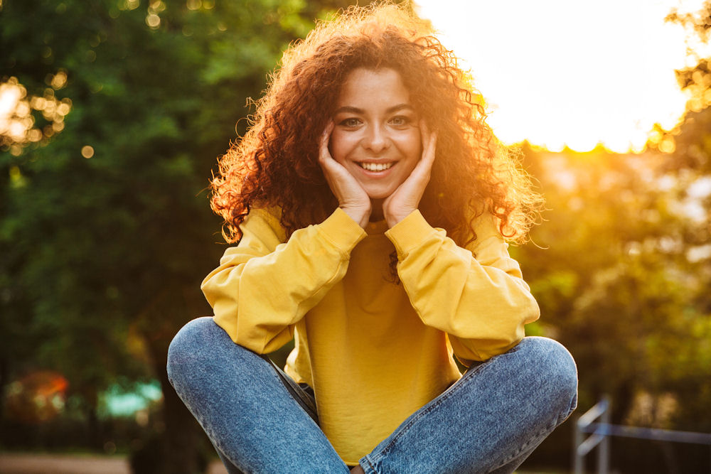 woman sitting on ground, holding her face and smiling